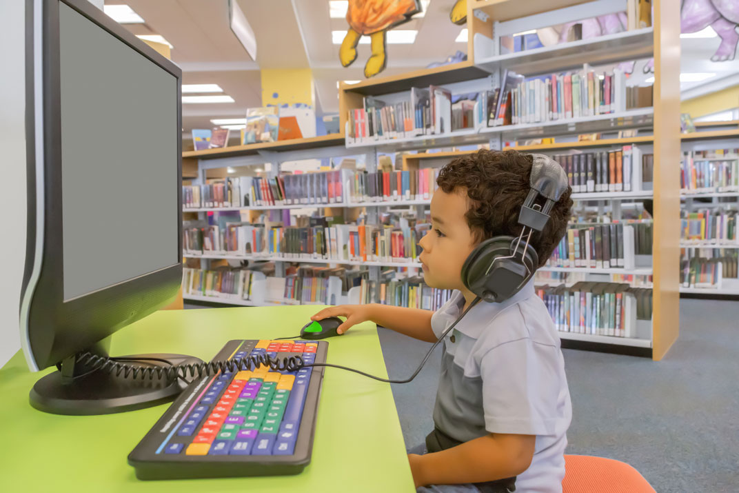 little boy on computer at the library with headphones on